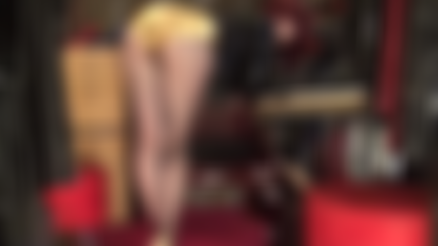 Mistress Vivian is bent over her table, looking back, teasing with her perfect ass in shiny gold satin shorts.
